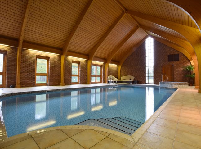 An indoor swimming pool with steps leading into the water wooden arched ceiling brick walls and lounge chairs at Solway in Chester