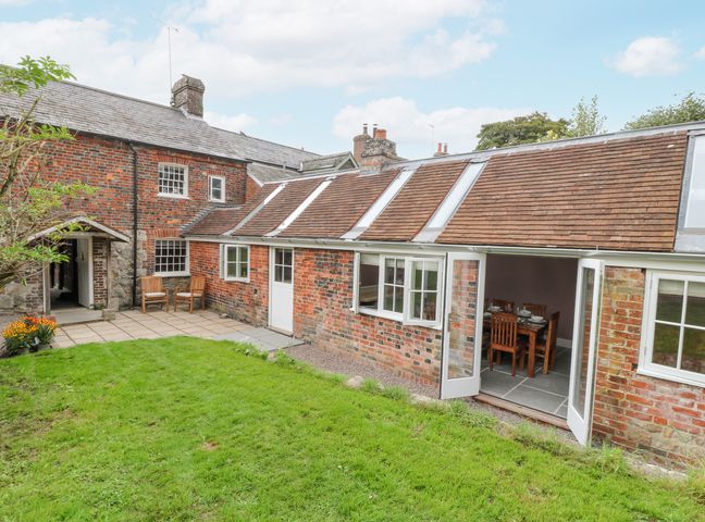 A brick house with a grass lawn and patio chairs outside the door at The Old Bakehouse in Avebury