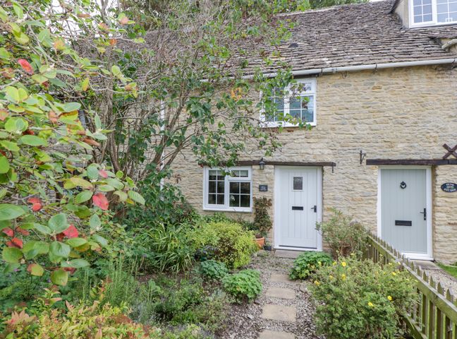 Stone cottage with white doors and windows surrounded by a garden and plants at Thorn Cottage in Fairford