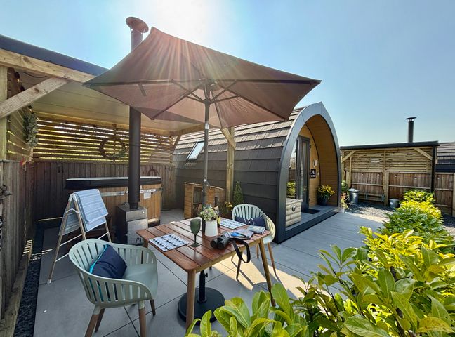 A patio with a table chairs umbrella and a wooden pod with a hot tub at Oh Deer in Ashbourne