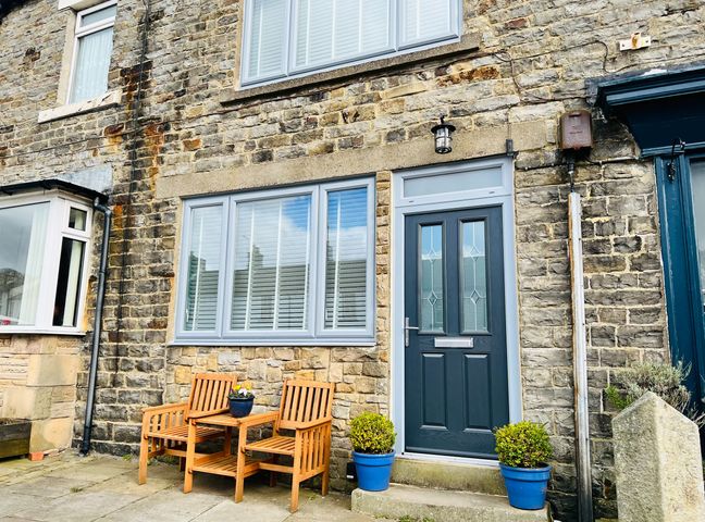 A stone house exterior with a dark door two wooden chairs a small table and potted plants at 15 Market Place in Middleton-In-Teesdale