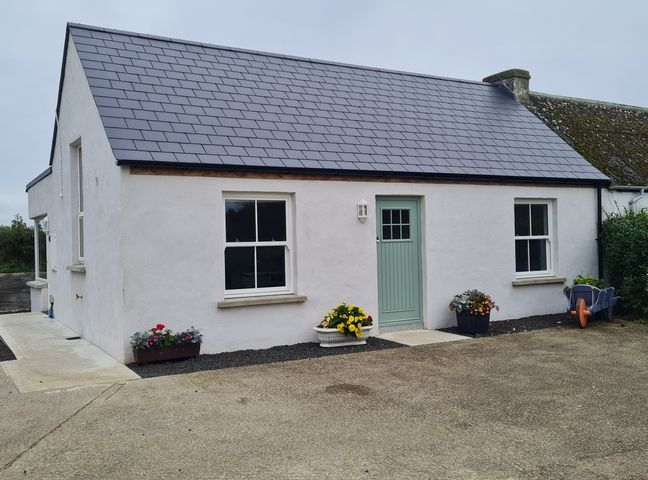 A small white house with a green door and two windows with flower pots outside at The Poets Cottage in Portglenone