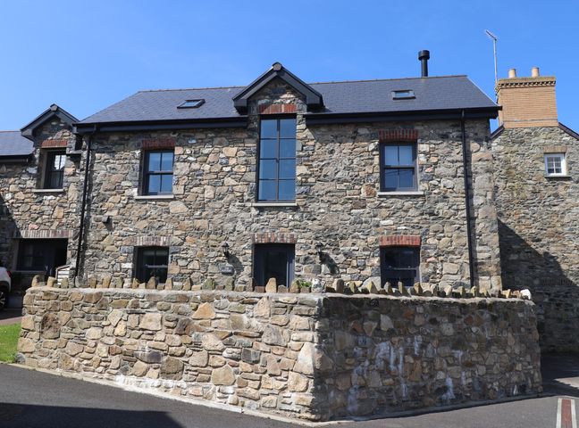 A stone house with black framed windows and a low stone wall in front at The Pottery in Newport Pembrokeshire