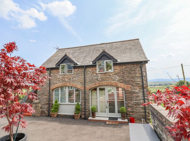 A stone house with arched windows and potted plants outside with red-leafed trees at Coach House in Clawdd-Newydd