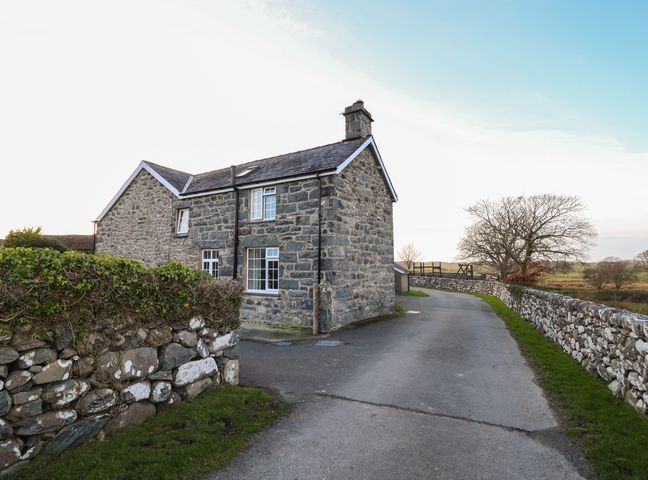 A stone house with a slate roof beside a paved road with stone walls and fields in the background at Ynys in Dyffryn Ardudwy