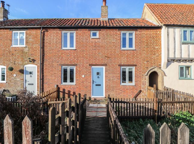 Front view of a brick terraced house with a blue door and windows surrounded by wooden fencing