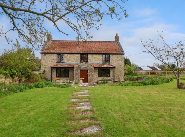 A stone house with tiled roof and wooden door with garden path and green lawn at Canny Croft in Chilton Polden near Street