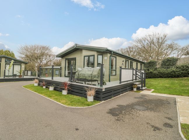A green lodge with a raised deck and potted plants beside a paved driveway at Gwydn Lodge in Downton Hampshire