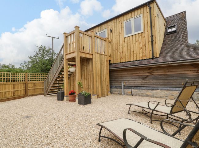 An outdoor area with wooden stairs leading to an upper floor and lounge chairs on gravel at The Attic at Redmond Bottom in Wookey