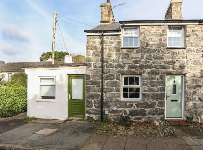 The front exterior of a stone house with mint green door and an attached white extension with a green door at Ty Eiddew Ivy House in Llanystumdwy near Criccieth
