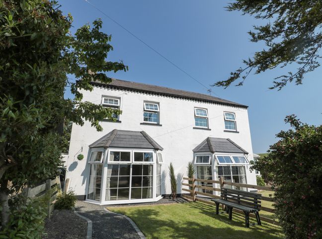 A white two-story house with bay windows a garden bench and a pathway at 9 Station Cottages in Belford