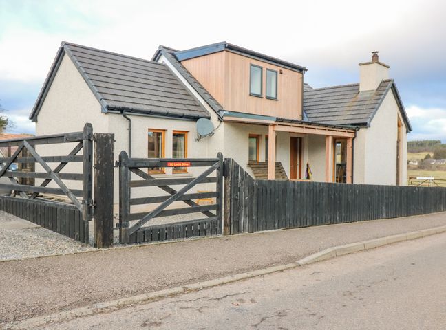 A house with a black wooden fence and gate along a paved road at Otakaro in Tomintoul