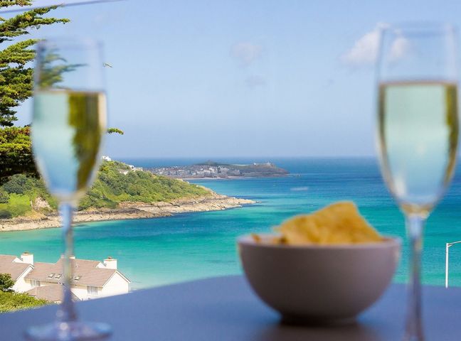 A coastal view with two glasses of champagne and a bowl of chips on a table at Sandsifters II in Carbis Bay