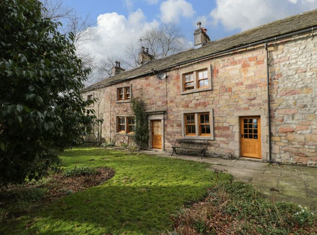 A stone house with wooden doors and windows with a grassy garden and bench at Bay Horse Farm in Skipton