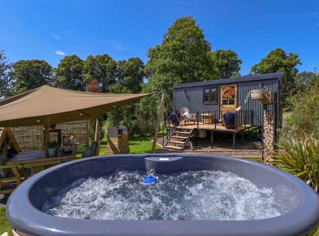A hot tub in front of a wooden cabin with outdoor seating and a canopy at Portland Luxury Glamping in Nottingham