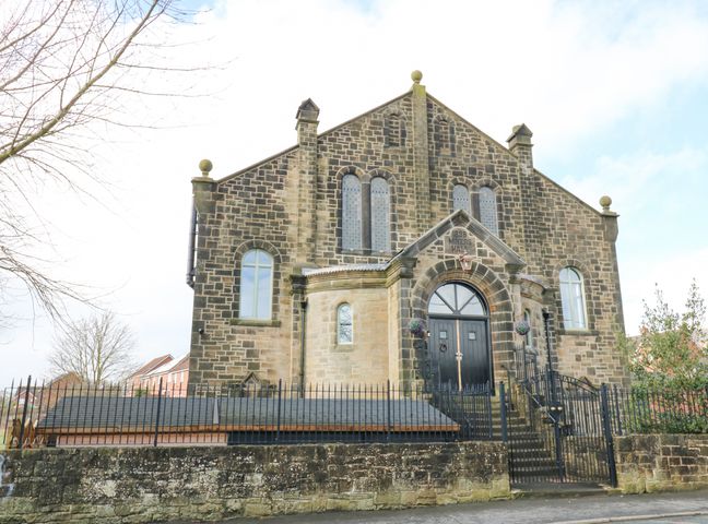 The exterior of a stone building with arched windows and a black door with steps and a black metal fence at The Miners Hall Retreat in Stanley County Durham