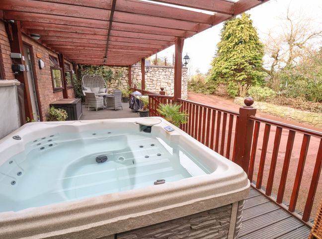 An outdoor covered patio with a hot tub a seating area and wooden railing at Acorns in Holywell