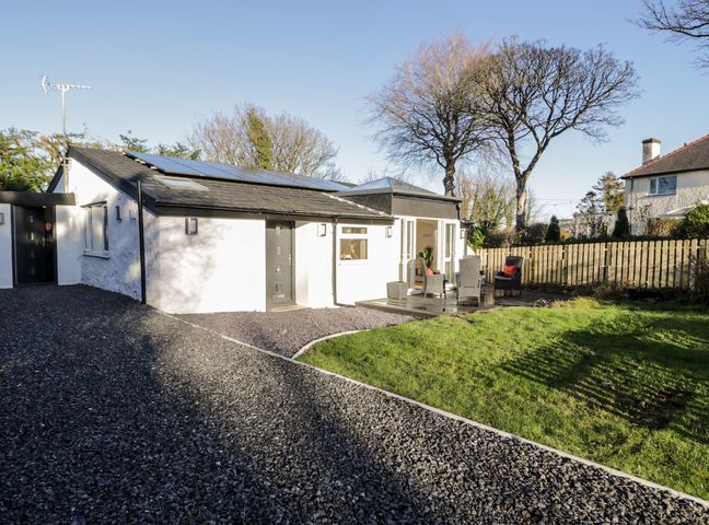 A single-story white house with a gravel driveway and outdoor seating area on a wooden deck at The Cottage at Cromlech Manor Farm in Llanfair-Mathafarn-Eithaf near Benllech