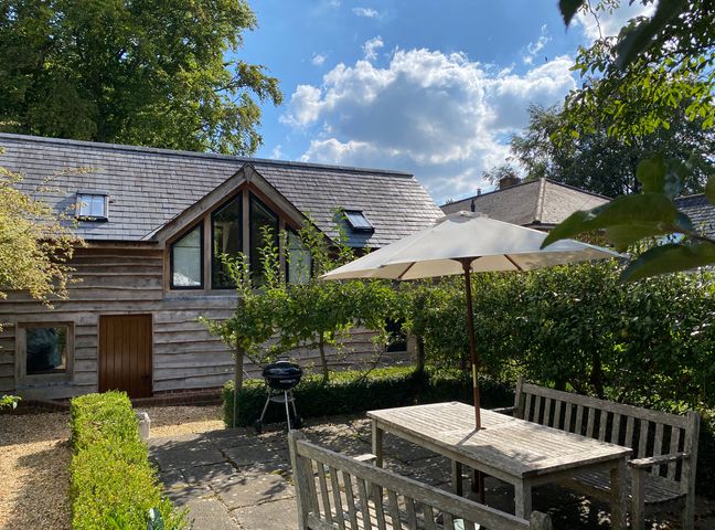 An outdoor patio with wooden table and benches under a white umbrella next to a small grill and a wooden house at Avon Turn View in Alderbury