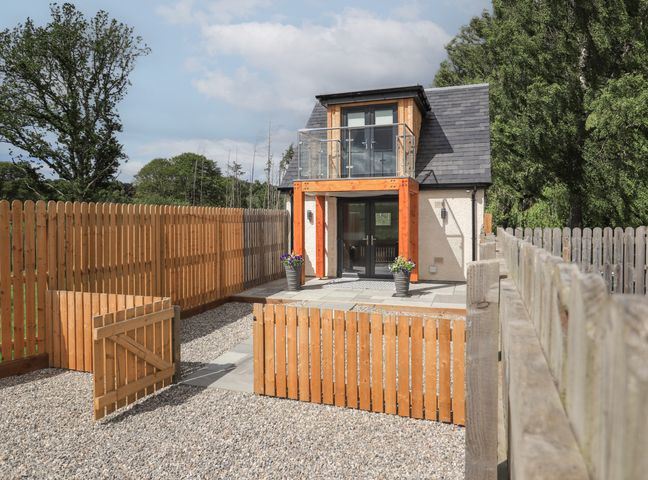 A small two-story house with a wooden fence and gate in front at Wee Smithy in Munlochy