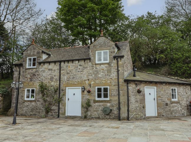 A stone cottage with white doors and windows surrounded by trees at The Old Hall in Halkyn near Holywell