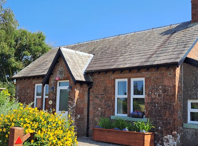 Exterior view of a stone cottage with a slate roof yellow flowers and planters near the entrance at Bogrie Cottage in Canonbie near Gretna Green