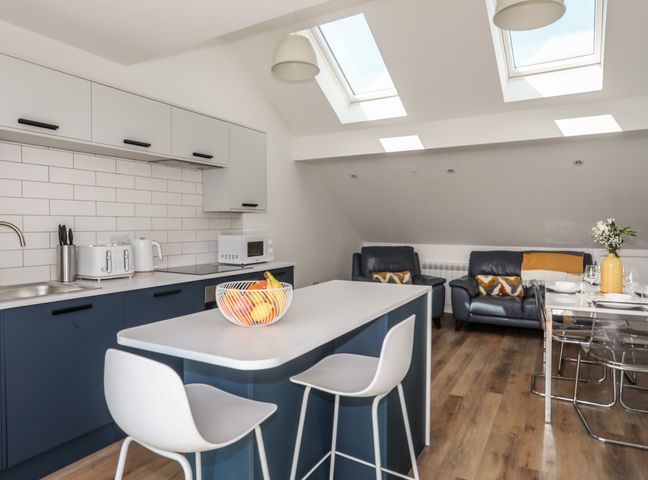A kitchen with island and stools next to a living area with sofas and a dining table at Golygfa'r Gastell Castle View in Criccieth