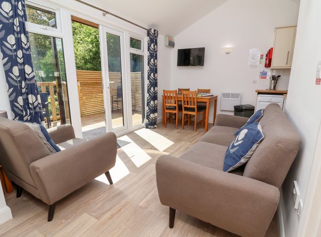 A living area with two armchairs and a sofa near glass doors and a dining table with four chairs at Chalet Log Cabin C9 in Combe Martin