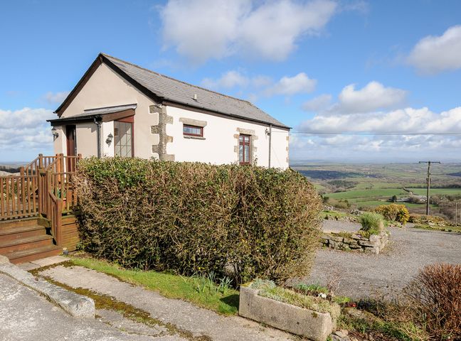 An exterior view of a small house with hedge and wooden stairs overlooking fields at Cheesewring Cottage Minions near Upton Cross