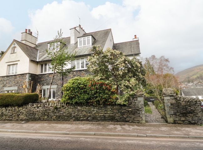 A house with stone walls and multiple windows behind a stone fence with a metal gate at Connies Cottage in Ambleside