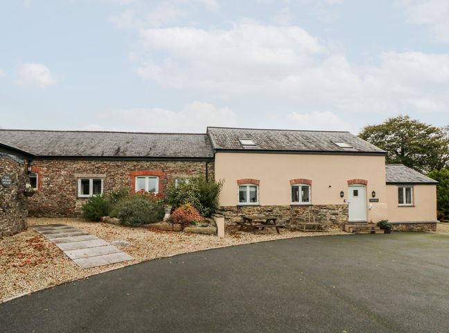 A stone and plaster house with a paved path and gravel garden beds with shrubs and picnictable at Hare Barn in Lifton