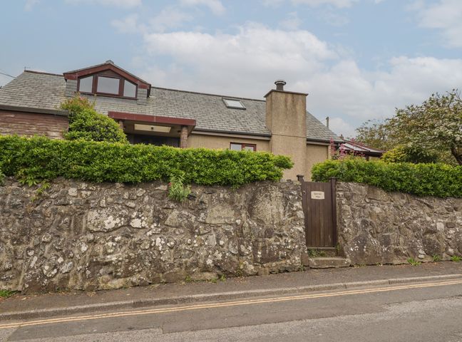 A house with a stone wall and green hedge with a wooden gate at Spernenwyn in St Ives