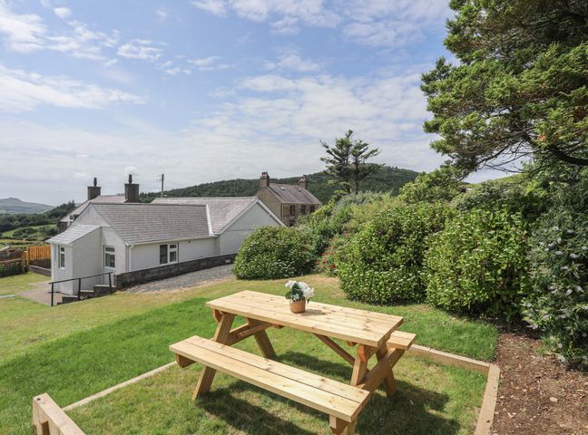 A wooden picnic table with a flower pot on grass with houses and trees in the background at Glan Awel in Nefyn