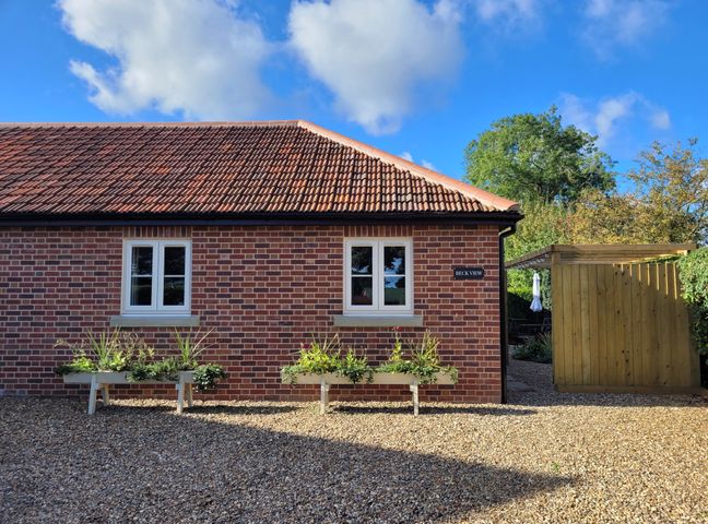 A brick building with two white windows and two flower planters outside at Beck View Weston Longville near Lenwade
