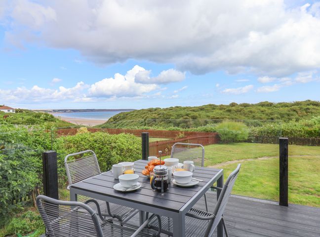 An outdoor patio with a table set for breakfast overlooking green bushes and a beach at 29 Gap Road in Hunmanby