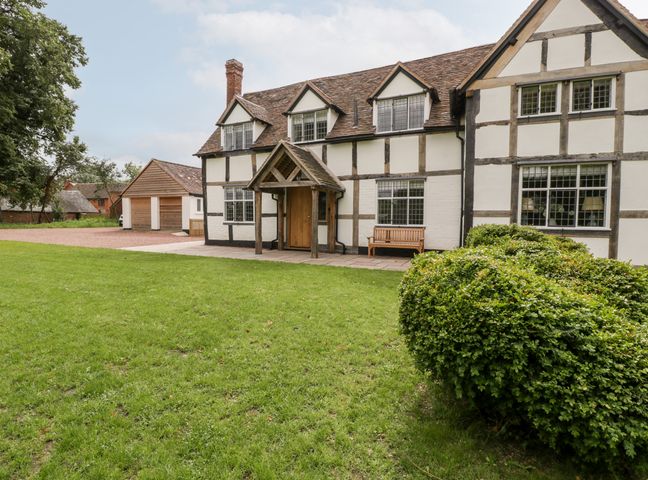 A traditional house with timber framing a wooden bench and green lawn at Byways in Madresfield near Malvern