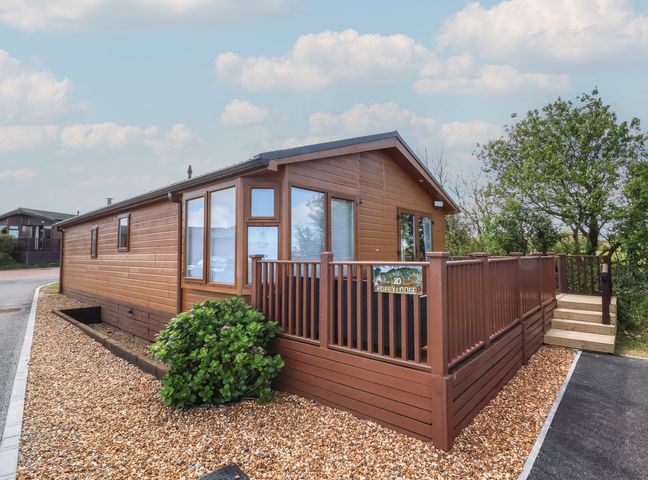 A brown wooden lodge with a deck and railing surrounded by gravel at Poppy Lodge in Mullacott Ilfracombe