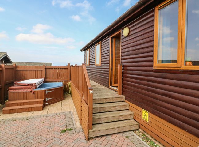 An exterior view of a wooden cabin with stairs leading to an open door next to a hot tub on a paved area at Seascape Retreat in Ilfracombe