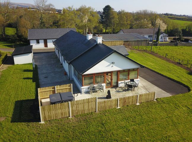 A single-story house with a fenced patio area and outdoor furniture in a rural setting at Rose Cottage in Muff County Donegal