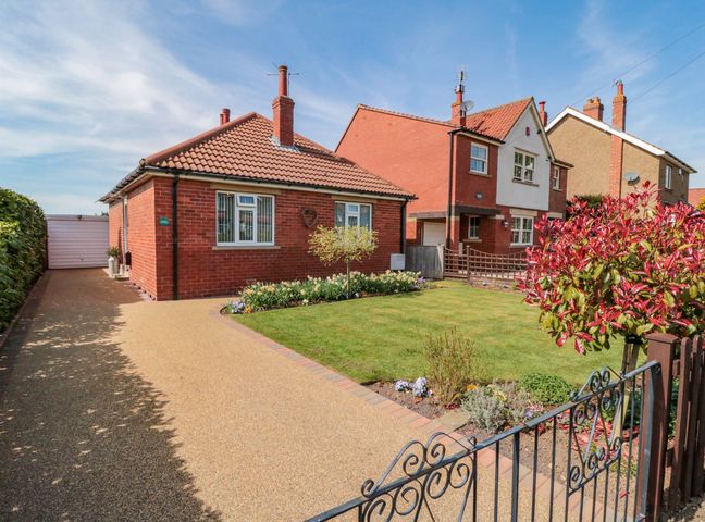 A front yard with a driveway garage lawn flowers and two brick houses at Field Cottage in Kirkbymoorside