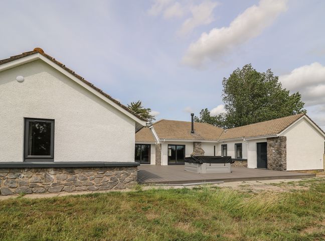 An exterior view of a single story house with stone and white walls and a wooden deck at Heritage in St Clears