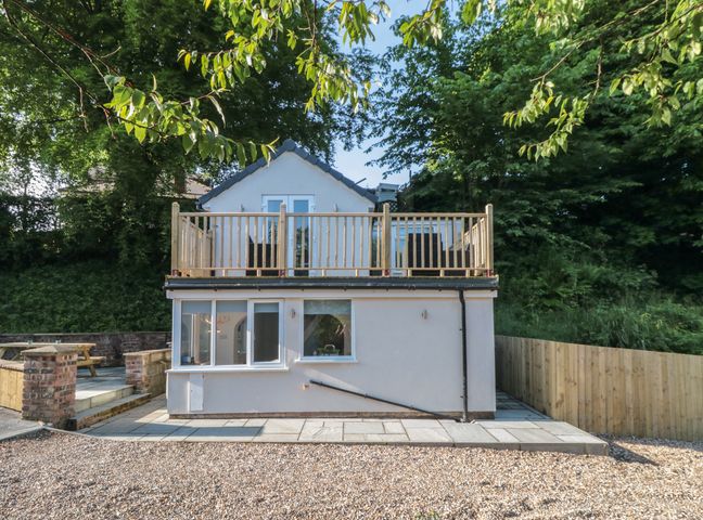 A two-story house with a wooden balcony surrounded by trees and a gravel area at Riverside Cottage in Scarborough