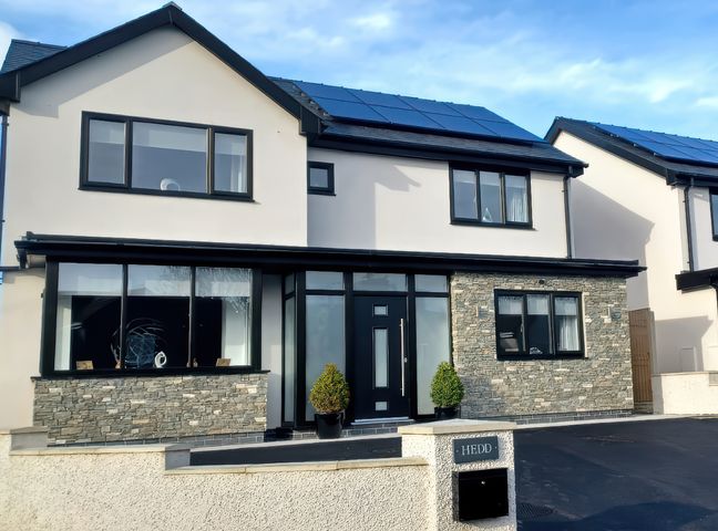 A modern two-story house with stone and white exterior walls solar panels on the roof and a black front door at Hedd in Amlwch
