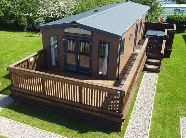 A wooden cabin with a large deck surrounded by grass at Mayflower Lodge in Runswick Bay near Staithes