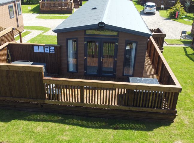 A wooden cabin with a fenced porch and patio furniture in a grassy area