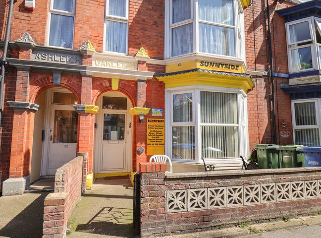 Front of a brick building with arch doorways and a bay window with a yellow sign for Sunnyside Holiday Apartments in Bridlington