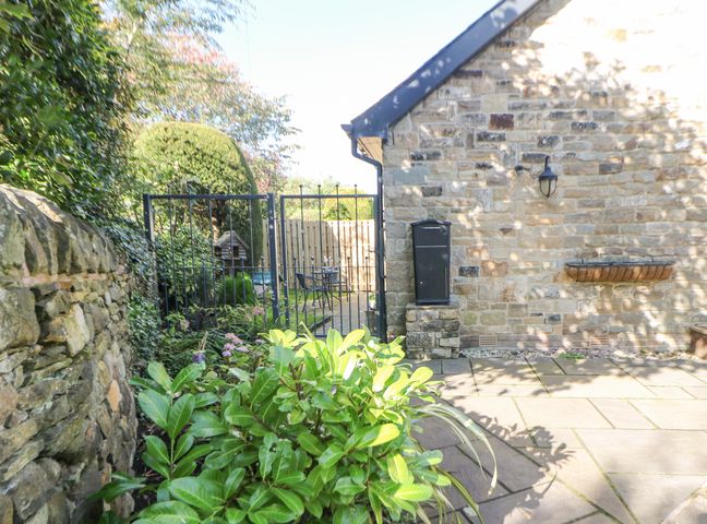 A stone wall with plants in front and a metal gate leading to a patio with a table and chairs at Causeway Hideaway in Dore