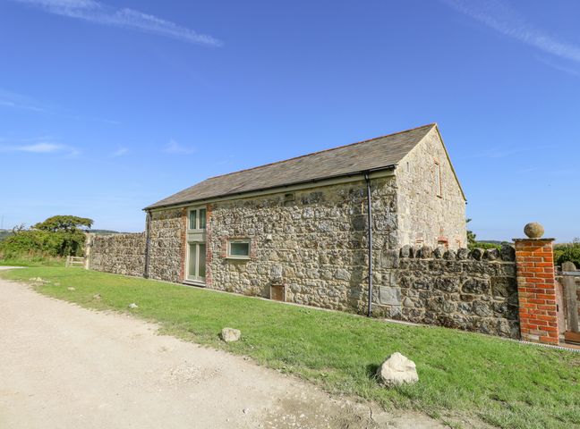 A stone barn with a pitched roof next to a dirt path and a low stone wall at Garstons Barn in Gatcombe near Newport Isle Of Wight