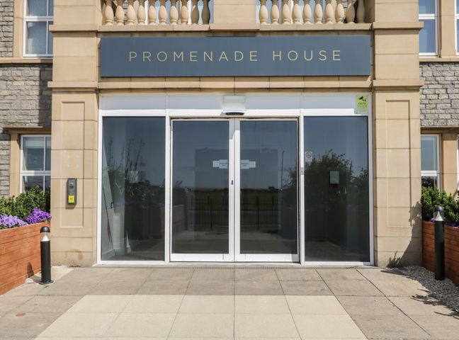 Glass entrance doors to Promenade House with stone columns and planters with flowers on either side