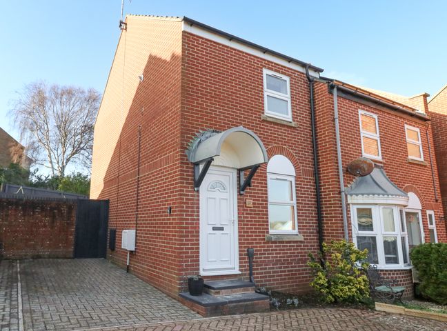 A brick end terrace house with a white door and windows and a paved driveway at The Nightingale in Weymouth